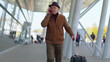 © Andrii Iemelianenko - Senior tourist grandfather walking on international airport hall, railway station carrying luggage suitcase talking on smartphone and smiles. Travel, vacation. Pensioner businessman using mobile phone