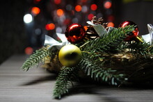 Christmas Decoration A Sprig Of A Christmas Tree, A Pine Cone And Christmas Decorations On A Straw Ring Against A Background Of Flickering Red Lights. Christmas Decoration On A Dark Wooden Background.