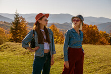 Outdoor Autumn Fashion Portrait Of Two Young Confident Women Wearing Stylish Outfits With Hats, Sunglasses, Bags, Denim Clothes, Posing, Walking In Mountains. Copy, Empty Space For Text