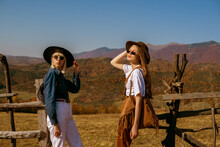 Two Young Confident Women Wearing Stylish Autumn Outfits With Hats, Sunglasses, Bags, Posing In Mountains. Outdoor Fashion Portrait. Copy, Empty Space For Text
