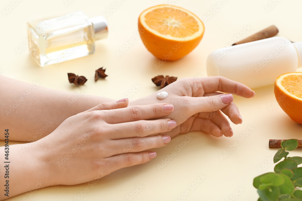 Woman applying cosmetic cream onto hands against light background