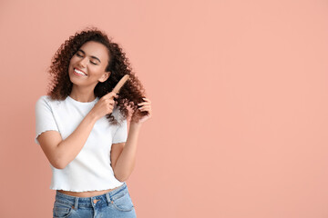 Young African-American woman combing her hair on pink background