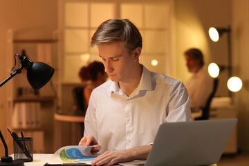 Wall Mural - Young businessman working with documents in office at night