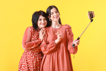 Sticker - Mature woman and her young daughter taking selfie on yellow background