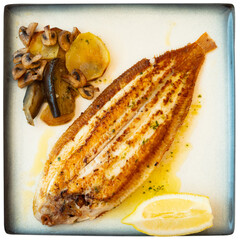 Grilled common sole served with wedge of fresh lemon and vegetable garnish of baked potato, eggplant and mushrooms. Isolated over white background