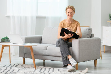 Canvas Print - Young woman reading Holy Bible on sofa at home