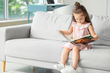 Sticker - Adorable little girl reading book on sofa at home