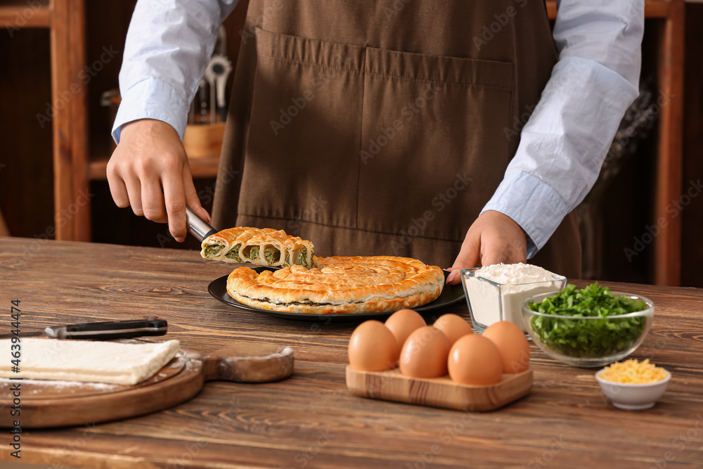 Woman taking slice of spinach pie at table in kitchen, closeup