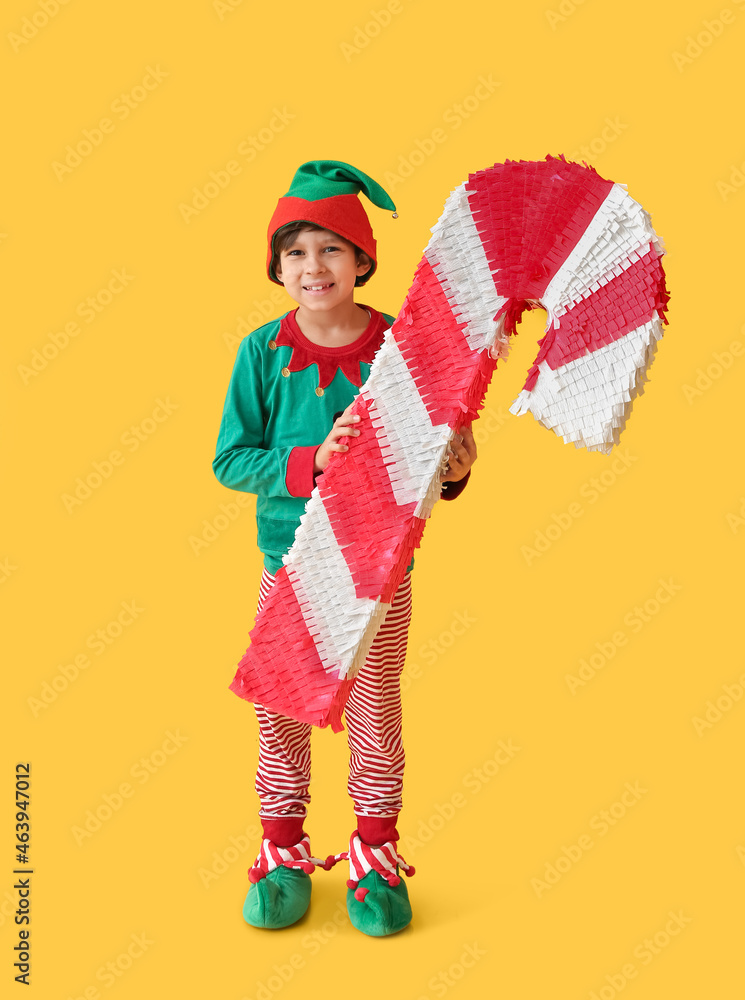 Cute little boy dressed as elf with candy cane pinata on color background