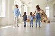 © Studio Romantic - Family standing in empty unfurnished spacious living room, rear view, from behind. Mom, dad and kids carrying and unpacking boxes together while moving into house or apartment. Buying new home concept