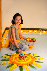 Wall Mural - Cute indian little girl making decoration with flower and oil lamp for diwali festival at home.