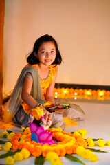 Wall Mural - Cute indian little girl making decoration with flower and oil lamp for diwali festival at home.