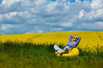 Sticker - Beautiful female in rainbow LGBT suspenders for pants sitting in bean chair in rapeseed field