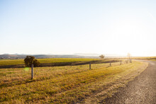 Sunlit Country Road And Rural Farm Paddocks And Fence