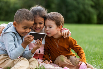 Wall Mural - childhood, leisure and technology concept - happy children with smartphone sitting on blanket at park