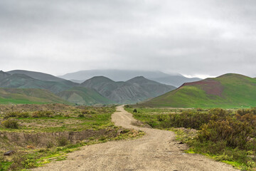 Wall Mural - Dirt road in a mountainous area in cloudy weather