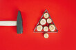Long nails and wood cuts or branch slabs, laid out in shape of Christmas tree with hammer on red background, flat lay