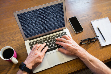 Hands of caucasian male programmer sitting at desk, using laptop with coding on screen