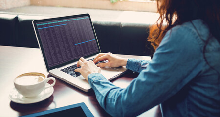 Caucasian female programmer sitting at desk with coffee, using laptop with coding on screen
