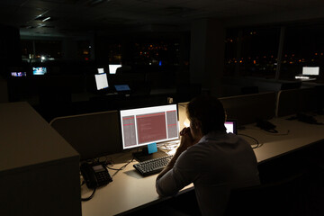 caucasian male programmer sitting at desk, using computer with coding on screen