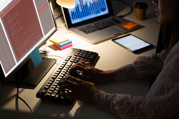 Biracial female programmer sitting at desk, using computer with coding on screen