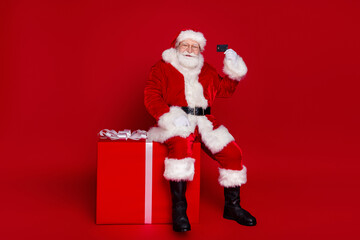 Wall Mural - Photo of handsome positive retired man wear santa claus costume spectacles smiling buying credit card present isolated red color background