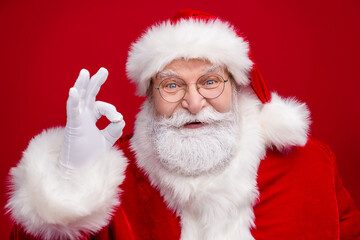 Wall Mural - Photo of funny excited retired man wear santa claus costume spectacles smiling showing okey sign isolated red color background