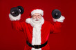 © deagreez - Photo of funny confident man pensioner dressed santa claus costume building arms muscles smiling isolated red color background