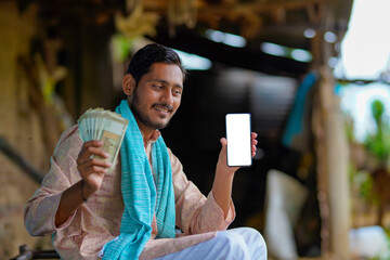 Wall Mural - Indian farmer showing smartphone and money at home.