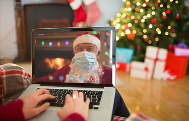 Poster - Caucasian woman on christmas laptop video call with caucasian santa wearing face mask