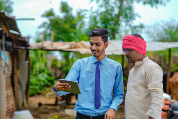 Canvas Print - Young indian agronomist showing some detail to farmer in smartphone at dairy farm