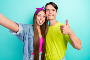 Poster - Photo of optimistic brunette young couple do selfie tongue out wear yellow pink t-shirts jeans isolated on teal color background