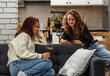 © Barillo_Images - Two young women relax at home and drink wine, one woman showing something on her smartphone to another one.