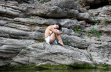 pensive young woman almost naked sitting on a rock near the river