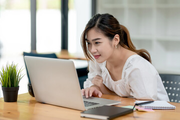 Wall Mural - Image of young Asian businesswoman sitting at the office looking at a laptop screen with documents at the desk.