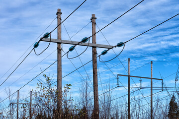 Power supply line with three wires mounted on old wooden pillar, blue sky with soft white clouds at background