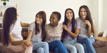 Group Of Happy Multiracial Female Friends Sitting On Sofa, Telling Funny Jokes And Laughing. Multiethnic Young Women Spending Time At Home, Talking, Sharing Positive Emotions And Having Fun Together