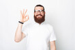 Young bearded man is showing ok gesture over white background.