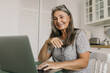 © shurkin_son - Good-looking, charming grand-mother having online video conversation with her daughter and grandchildren using green laptop, smiling keeping glasses on grey head, while pie is being cooked in oven