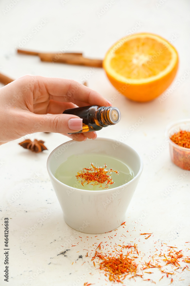 Woman adding essential oil to water in bowl on white background