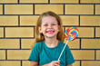 Happy girl with lollipop. A funny child is playing cheerfully. Sweet candy in childhood. Celebration and birthday for children. Sugar and unhealthy food. Beautiful smile. Multicolored rainbow spiral.