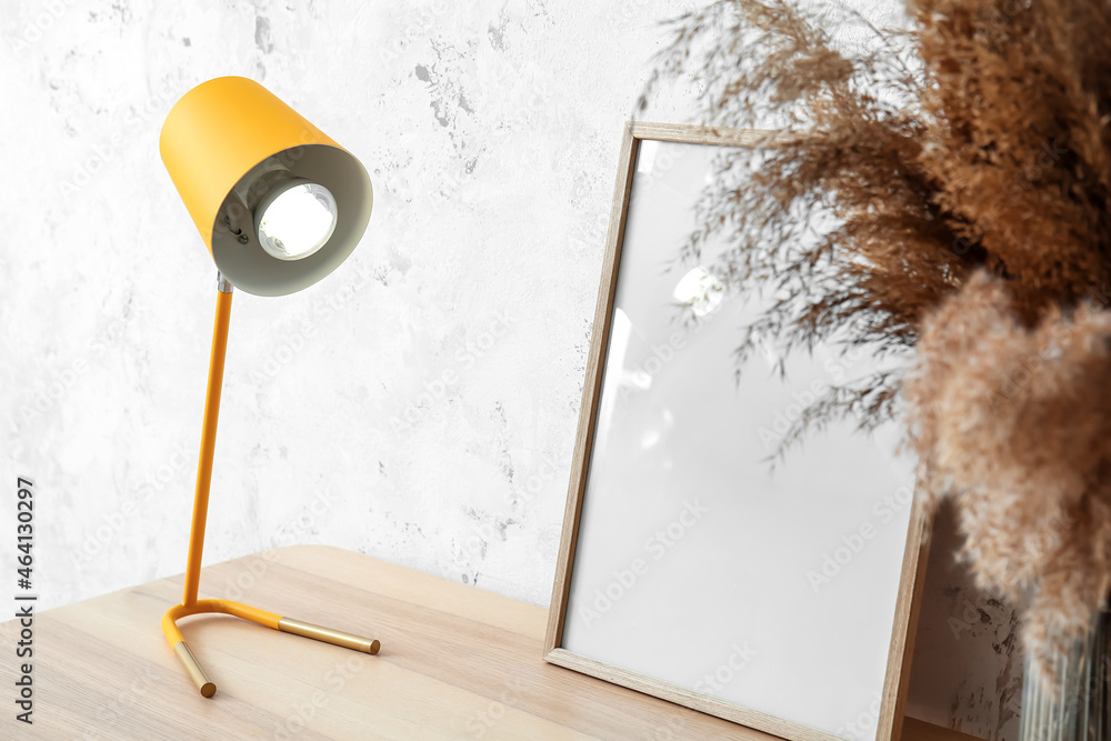 Blank frame with glowing yellow lamp on bench near light wall