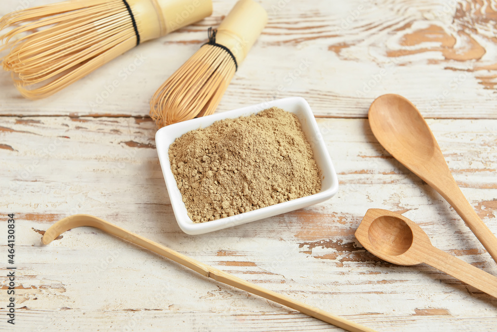 Bowl with hojicha powder, chasen and chashaku on white wooden background