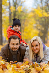 Wall Mural - Happy family laying on dry leaves and looking at camera