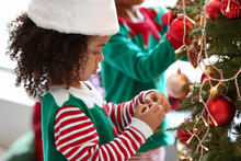 Little African-American Girl Dressed As Elf Decorating Christmas Tree At Home