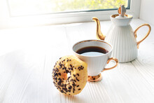 White Porcelain Teapot And Cup On Windowsill On Sunny Day. Banana Doughnut With Chocolate Chips For A Sweet Breakfast