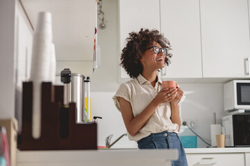 Wall Mural - Pretty Afro American woman in glasses standing in modern office kitchen interior