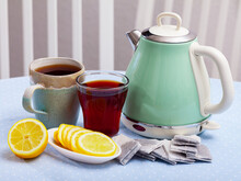 Tea Party For Couple. Retro Style Turquoise Electric Kettle, Two Cups Of Tea And Sliced Lemon On Wooden Kitchen Table..