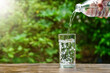 pouring water from the bottle into a glass on wooden in nature on green background. Concept of environment protection, healthy drink. 
