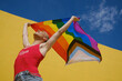 © alvaro - Cheerful non-binary person holding up and waving an lgbt pride flag outdoors.